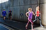 Four young adult runners running along city sidewalk