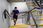 Young male runner running up indoor stairway