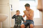 Boy in bathroom with father brushing teeth together