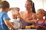 Mature woman and children blending fresh smoothie in kitchen