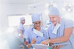 Surgeons with digital tablet discussing paperwork on clipboard in operating room