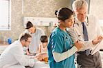 Male doctor and female nurse making rounds, reviewing medical record in hospital room