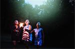 Three girls holding sparklers looking up from garden at night on independence day, USA