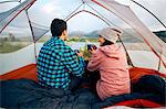 Couple sitting in tent, drinking hot drinks, looking at view