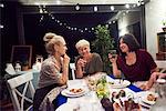 Three women sitting at dinner table, drinking from wine glasses