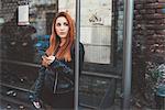 Red haired woman waiting at bus stop holding smartphone