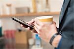 Hands of businessman holding coffee cup and smartphone