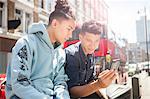 Two young men outdoors, looking at smartphone
