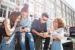 Four young friends outdoors, looking at smartphone