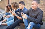 Four friends sitting in street, looking at smartphones