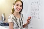 Portrait smiling, confident girl student solving physics equation at whiteboard in classroom