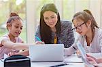 Female teacher and girl students researching at laptop in library