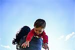 Low angle view of male toddler over mother's shoulder against blue sky