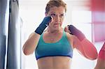 Determined female boxer with wrist wraps in fighting stance at gym