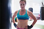 Portrait confident, tough female boxer standing at punching bag in gym