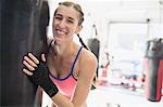 Portrait smiling, confident young female boxer at punching bag in gym
