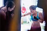 Determined, tough female boxers boxing at punching bag in gym
