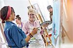 Smiling female artists with paintbrushes and palettes painting in art class studio