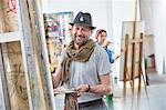 Portrait smiling male artist painting at easel in art class studio