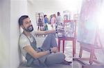 Portrait smiling male artist with palette painting at easel in art class studio