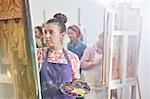 Focused female artist with palette painting at easel in art class studio