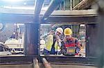 Male engineers with laptop examining parts in factory