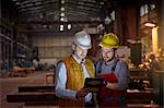 Male foreman and engineer using digital tablet in dark factory