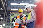 Male foreman and worker with clipboard talking in factory