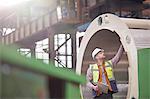 Male engineer with clipboard examining steel pipe in factory