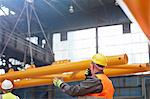 Male worker with walkie-talkie guiding lowering of equipment in factory