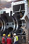 Male workers examining large steel equipment in factory