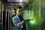 Male IT technician holding glowing futuristic digital tablet in server room