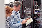 IT technicians with clipboard examining panel in server room