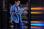 Focused male IT technician using digital tablet at panel in dark server room