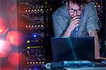 Focused male IT technician working at laptop in dark server room