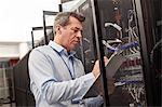 Male IT technician writing on clipboard at panel in server room