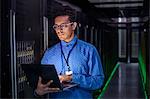 Focused male IT technician using laptop in dark server room