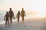 Family in wet suits walking with surfboards on sunny summer sunset beach