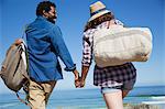 Multi-ethnic couple holding hands, walking on sunny summer ocean beach
