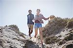 Playful, energetic multi-ethnic couple running on sunny summer sand beach path