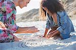 Mother and daughter drawing spirals in sand on summer beach