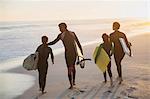 Family surfers walking with surfboards on sunny summer sunset beach