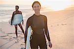 Portrait confident woman in wet suit with surfboard on sunny summer beach with family