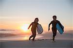 Brother and sister in wet suits running with boogie boards on summer sunset beach