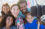 Smiling, happy multi-ethnic family taking selfie with selfie stick camera phone on beach