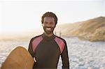 Portrait smiling, confident male surfer with surfboard on sunny summer beach