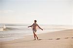 Carefree woman walking with arms outstretched on sunny summer ocean beach