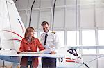 Pilot and engineer reviewing plans on airplane wing in hangar