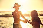 Playful young couple holding hands on sunny summer sunset ocean beach