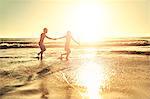 Young couple holding hands, walking in sunny summer sunset ocean beach surf